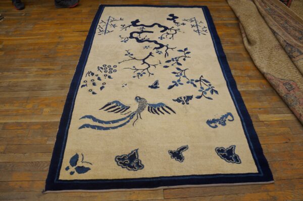 Beige rug with blue stylized bird, tree, and floral motifs, displayed on warm wooden flooring.