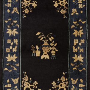 Black field rug with golden vase and floral motifs surrounded by a wide, indigo border pattern.