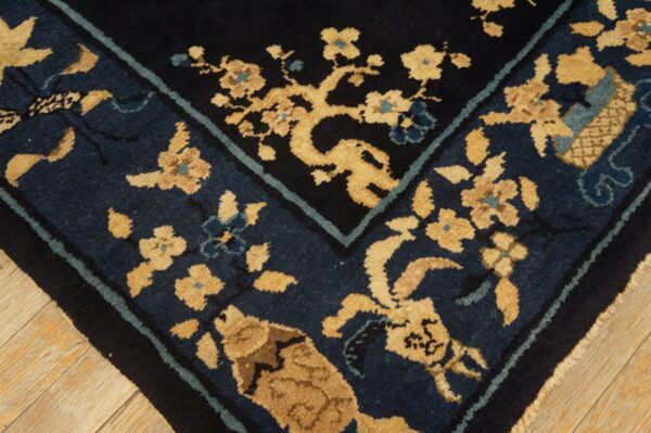 Dark blue and tan floral rug corner detail with a black border, visible over light wood flooring.