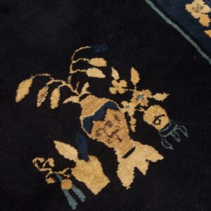 Black rug detail featuring a gold and blue stylized floral arrangement in a vase motif with a striped border.