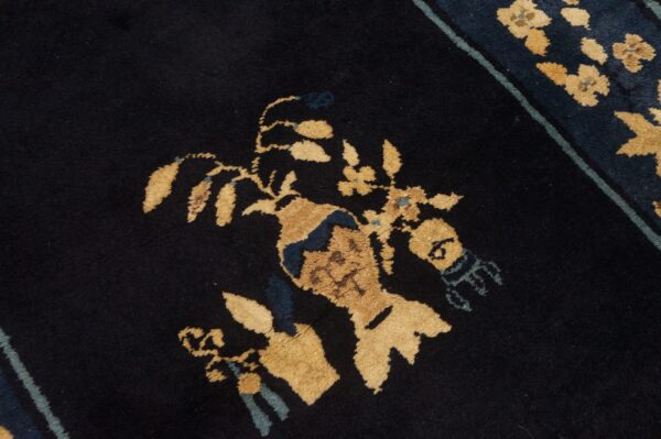 Black rug detail featuring a gold and blue stylized floral arrangement in a vase motif with a striped border.