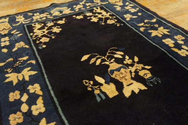 Dark blue rug detail with contrasting beige floral patterns and an ornate border on wooden flooring.