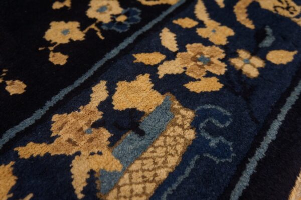 Textured, high-pile rug detail showing tan floral patterns on a dark blue field with light blue borders.