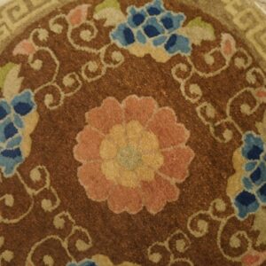Brown round rug with pink and blue floral medallion, scrolling vines, and a tan geometric border.