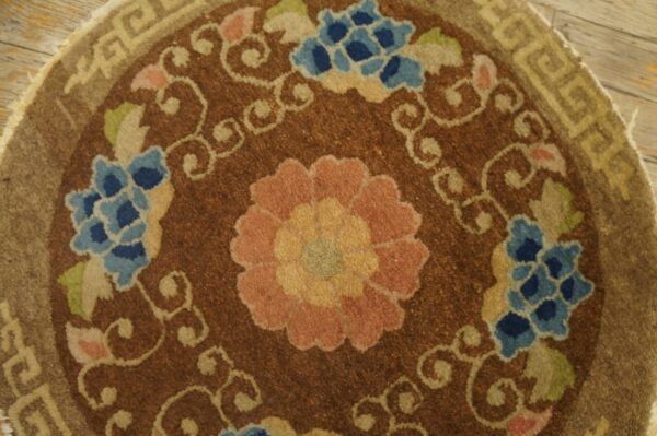 Brown round rug with pink and blue floral medallion, scrolling vines, and a tan geometric border.