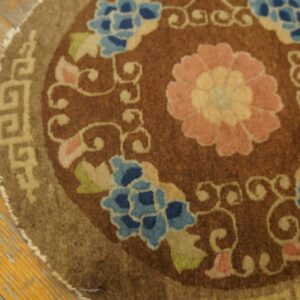 Round brown rug with pink floral medallion and blue flowers resting on distressed yellow wood planks.