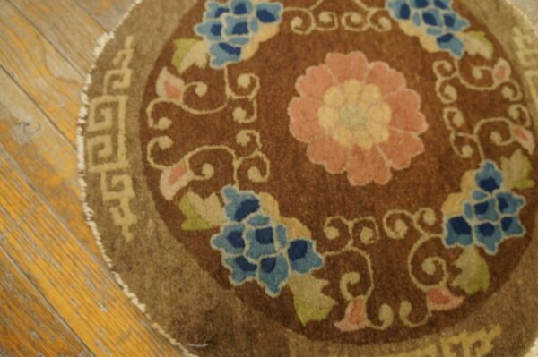 Round brown rug with pink floral medallion and blue flowers resting on distressed yellow wood planks.