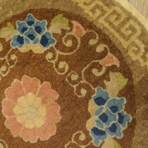 Brown rug detail showing blue and pink flowers, tan scrolling vines, and a geometric border on wood flooring.