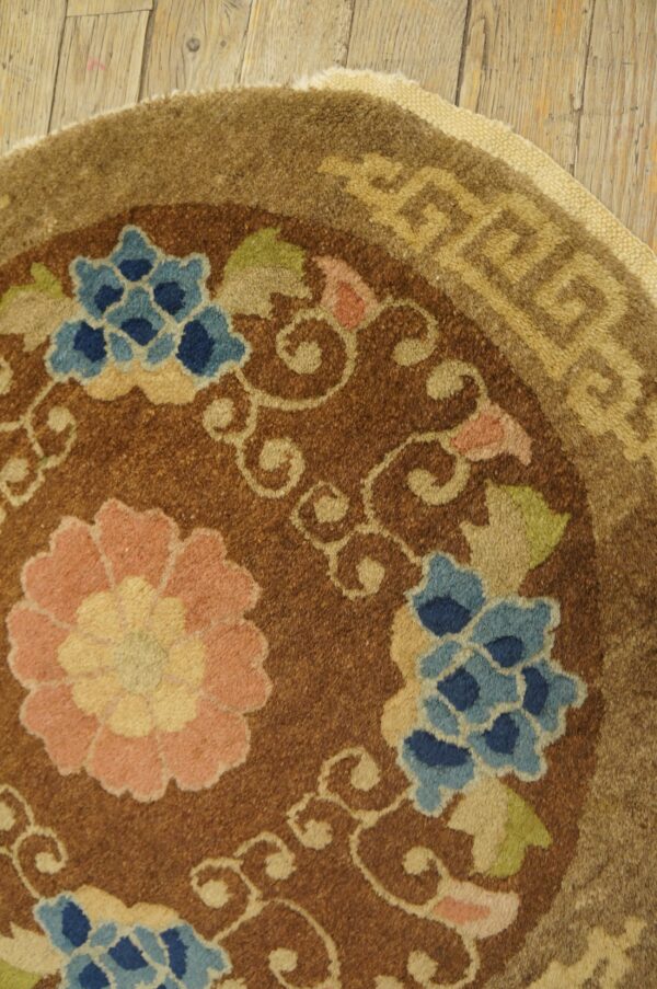 Brown rug detail showing blue and pink flowers, tan scrolling vines, and a geometric border on wood flooring.