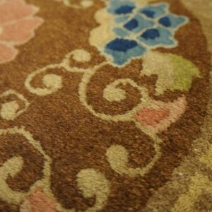 Brown rug detail showing textured pile with pink, blue, green, and tan floral scrollwork.