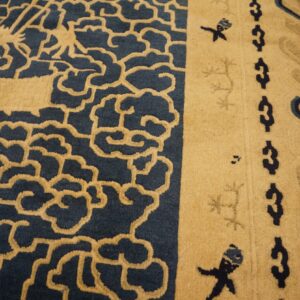 Sculpted high-pile rug in tan and navy blue with cloud patterns rests on distressed wooden floorboards.