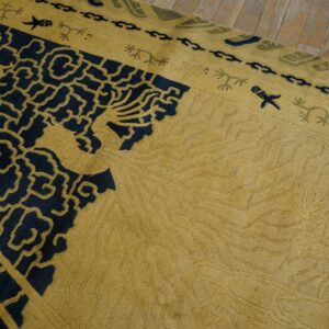 Carved gold and navy rug featuring detailed traditional patterns, viewed close-up on a wood floor.