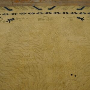 Light gold rug with carved water motifs and a navy blue border featuring stylized creatures rests on wood.