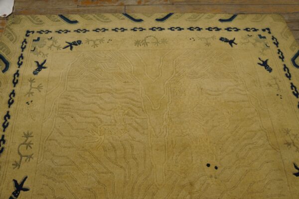 Light gold rug with carved water motifs and a navy blue border featuring stylized creatures rests on wood.
