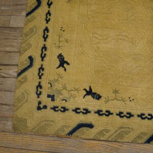 Golden yellow high-pile rug with navy and olive border motifs rests on distressed wood planks.