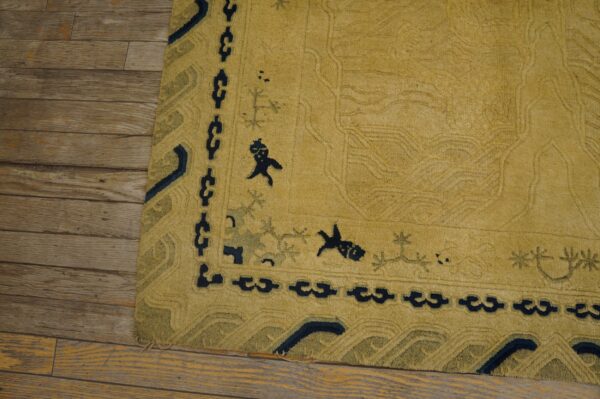 Golden yellow high-pile rug with navy and olive border motifs rests on distressed wood planks.