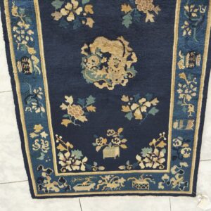 Dark blue rug with gold and teal traditional motifs, including a central medallion, shown on tile.