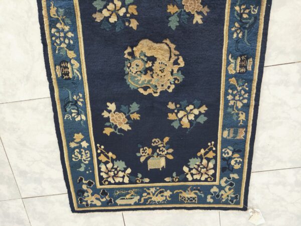 Antique peking small scatter size wool navy rug 2 Dark blue rug with gold and teal traditional motifs, including a central medallion, shown on tile.
