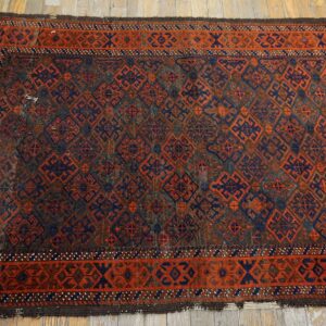 Traditional geometric rug in deep red-orange, navy blue, and brown on worn wood flooring.