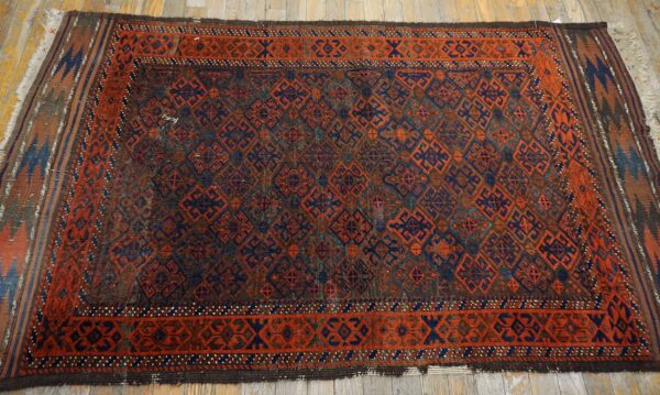 Traditional geometric rug in deep red-orange, navy blue, and brown on worn wood flooring.