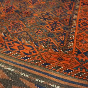 Detail of a rust and navy geometric rug featuring a main pile section and a striped flat woven end.