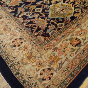 A detailed corner view of a densely patterned rug with navy blue, cream, and rust colors on wood floor.