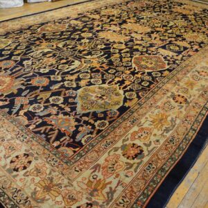 A large traditional rug with a navy center, colorful repeating motifs, and a wide beige border on wood floors.