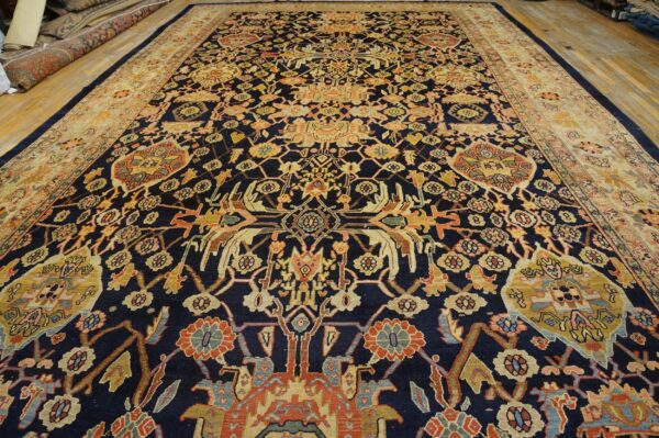 Navy blue rug with intricate gold and rust floral patterns and a wide beige border on wood floors.