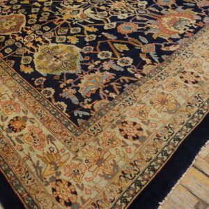 Ornate navy rug with floral motifs and a wide khaki border on distressed wooden flooring.