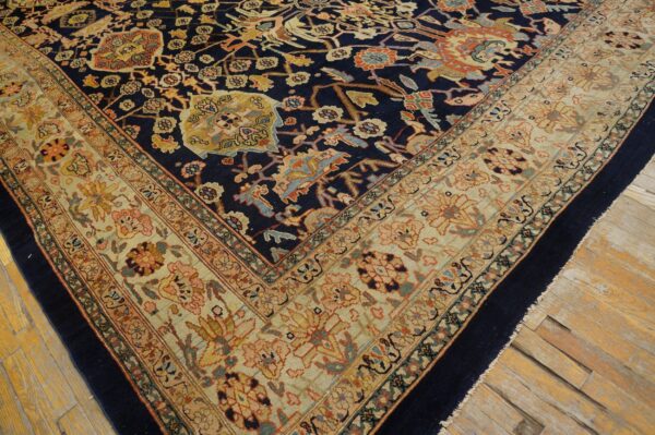 Ornate navy rug with floral motifs and a wide khaki border on distressed wooden flooring.