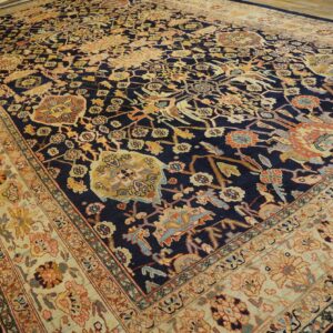 Ornate navy rug with colorful motifs and a contrasting light beige border rests on wood planks.