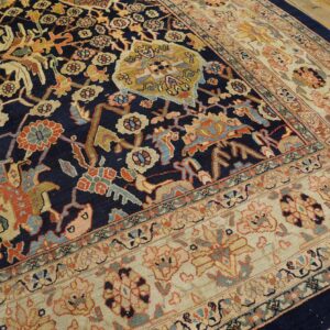 Ornate traditional rug featuring a navy field and multicolored floral patterns, bordered by cream, resting on wood floors.