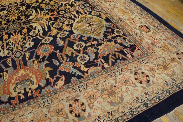Ornate traditional rug featuring a navy field and multicolored floral patterns, bordered by cream, resting on wood floors.