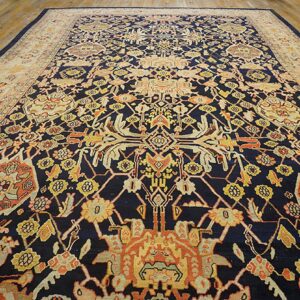 Intricate navy rug featuring gold and orange designs with a wide cream border on wooden floorboards.