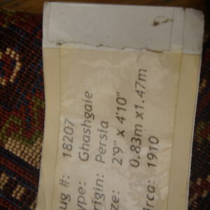 Low-pile geometric rug in red, blue, and cream with an attached label stating 100% wool pile.