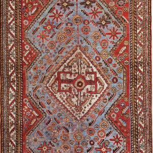 Traditional low-pile rug featuring a large geometric red and ivory medallion on a dusty blue field.