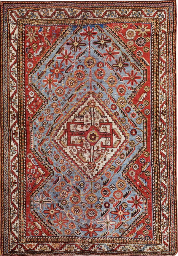 Traditional low-pile rug featuring a large geometric red and ivory medallion on a dusty blue field.