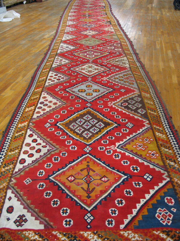 Vibrant red flatweave runner with complex multicolored geometric diamond patterns on light wood flooring.