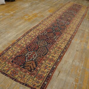 Long runner rug with navy, red, and tan botanical patterns centered on worn wooden plank flooring.