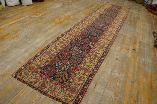 Long runner rug with navy, red, and tan botanical patterns centered on worn wooden plank flooring.