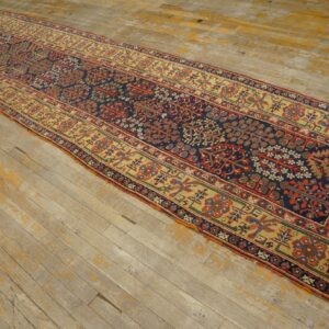 A long, low-pile runner rug with complex navy, red, and gold patterns lies on distressed wood flooring.