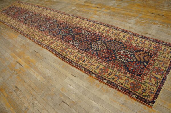A long, low-pile runner rug with complex navy, red, and gold patterns lies on distressed wood flooring.