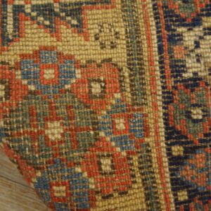 Detail of a low-pile geometric rug in golden beige, navy, red, and teal on wood flooring.