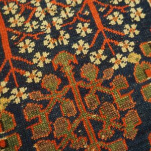 Close-up of a dark blue rug with stylized red vines, cream blossoms, and olive green geometric motifs.