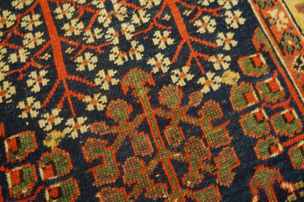 Close-up of a dark blue rug with stylized red vines, cream blossoms, and olive green geometric motifs.