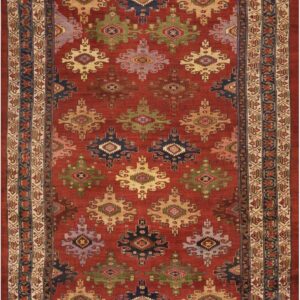 Red field rug patterned with large geometric motifs in olive, navy, beige, and lavender tones.