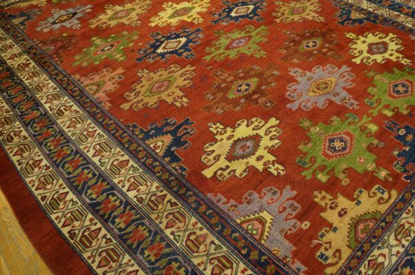 Red low-pile rug displaying multicolored geometric medallions and a detailed striped border over hardwood flooring.