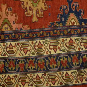 Detail of a rust-red traditional rug featuring geometric medallions and multi-layered borders resting on wood floor.