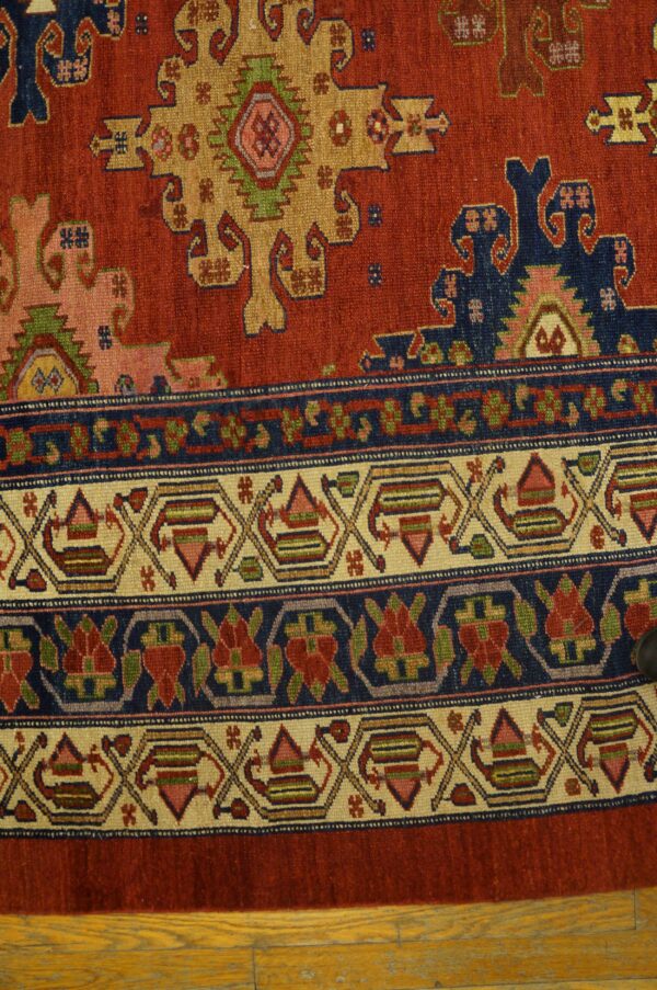 Detail of a rust-red traditional rug featuring geometric medallions and multi-layered borders resting on wood floor.