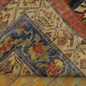 A patterned rug with red, navy, and beige elements is rolled back on light wood flooring.